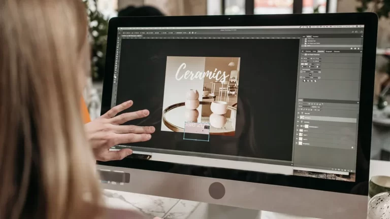 Projektant pracuje nad reklamową grafiką w programie na dużym monitorze.